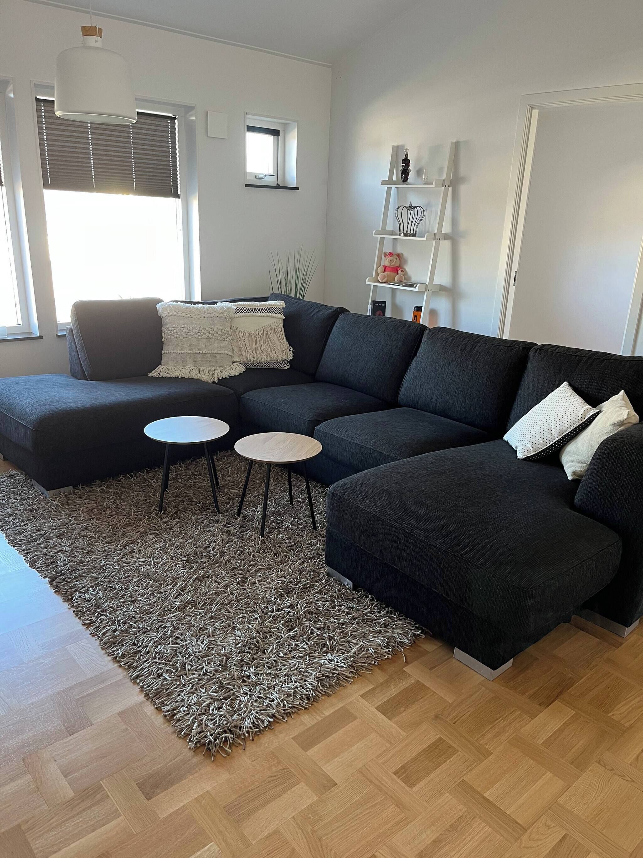 A modern living room with a sectional sofa, two small round tables, a patterned rug, and a wooden herringbone floor.
