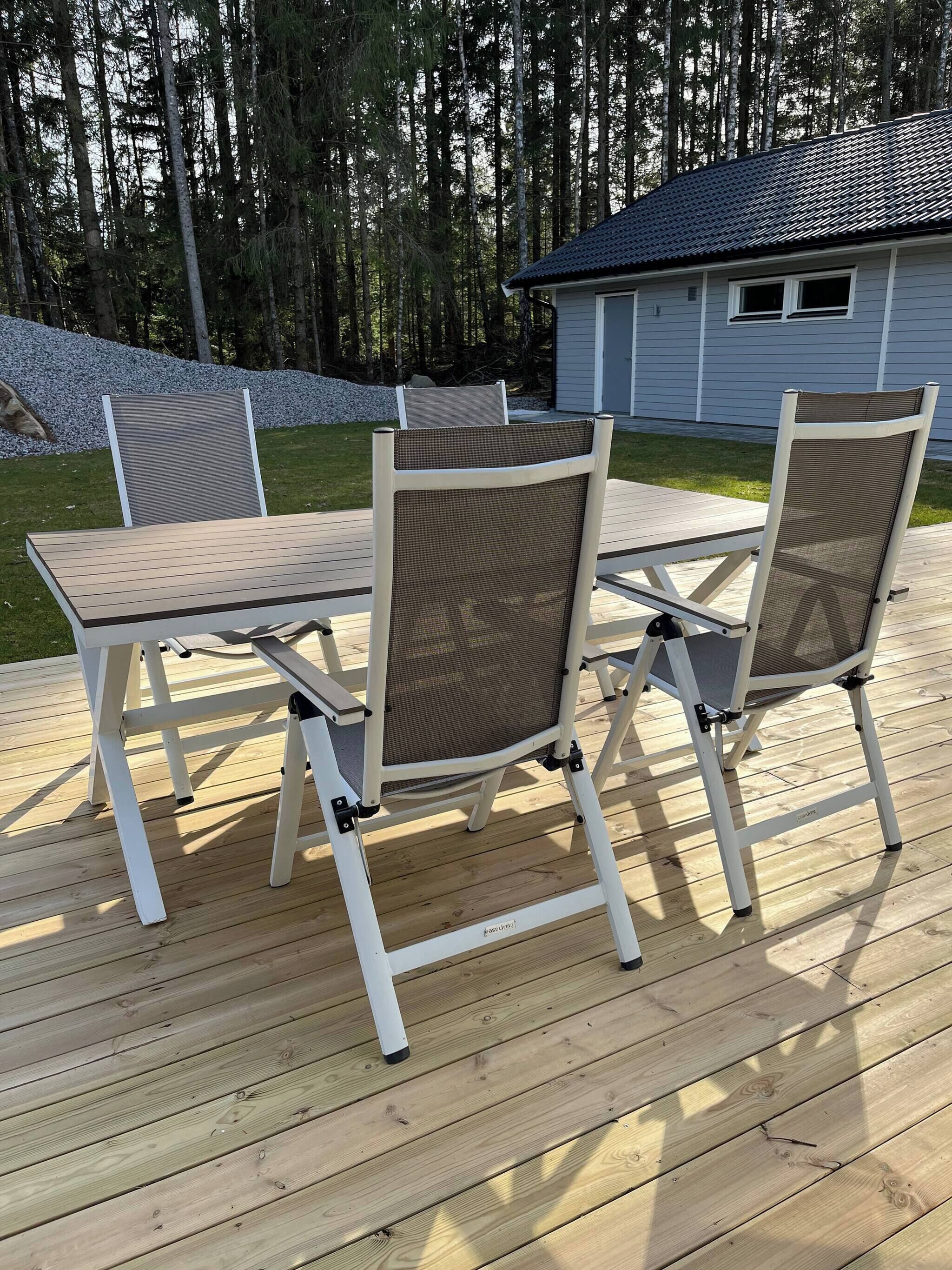 An outdoor deck with a table and chairs, surrounded by a wooden deck and a house in the background.