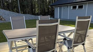 An outdoor deck with a table and chairs, surrounded by a wooden deck and a house in the background.