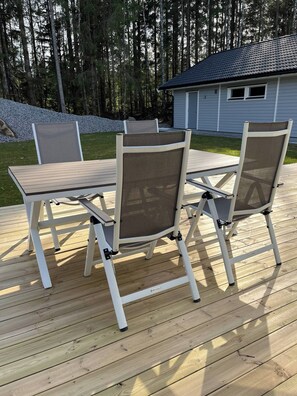 En uteplats med ett bord och stolar, omgiven av en träveranda och ett hus i bakgrunden.