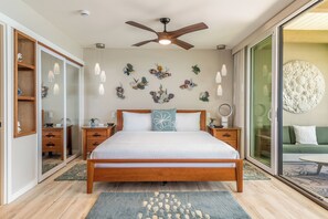 A bedroom with a wooden bed, a ceiling fan, a large wall art piece, and a sliding glass door leading to a balcony. - Beautiful Completely Renovated 2 Bed/2 Bath Oceanfront Gem - Kona Bali Kai #313 (Kailua-Kona)
