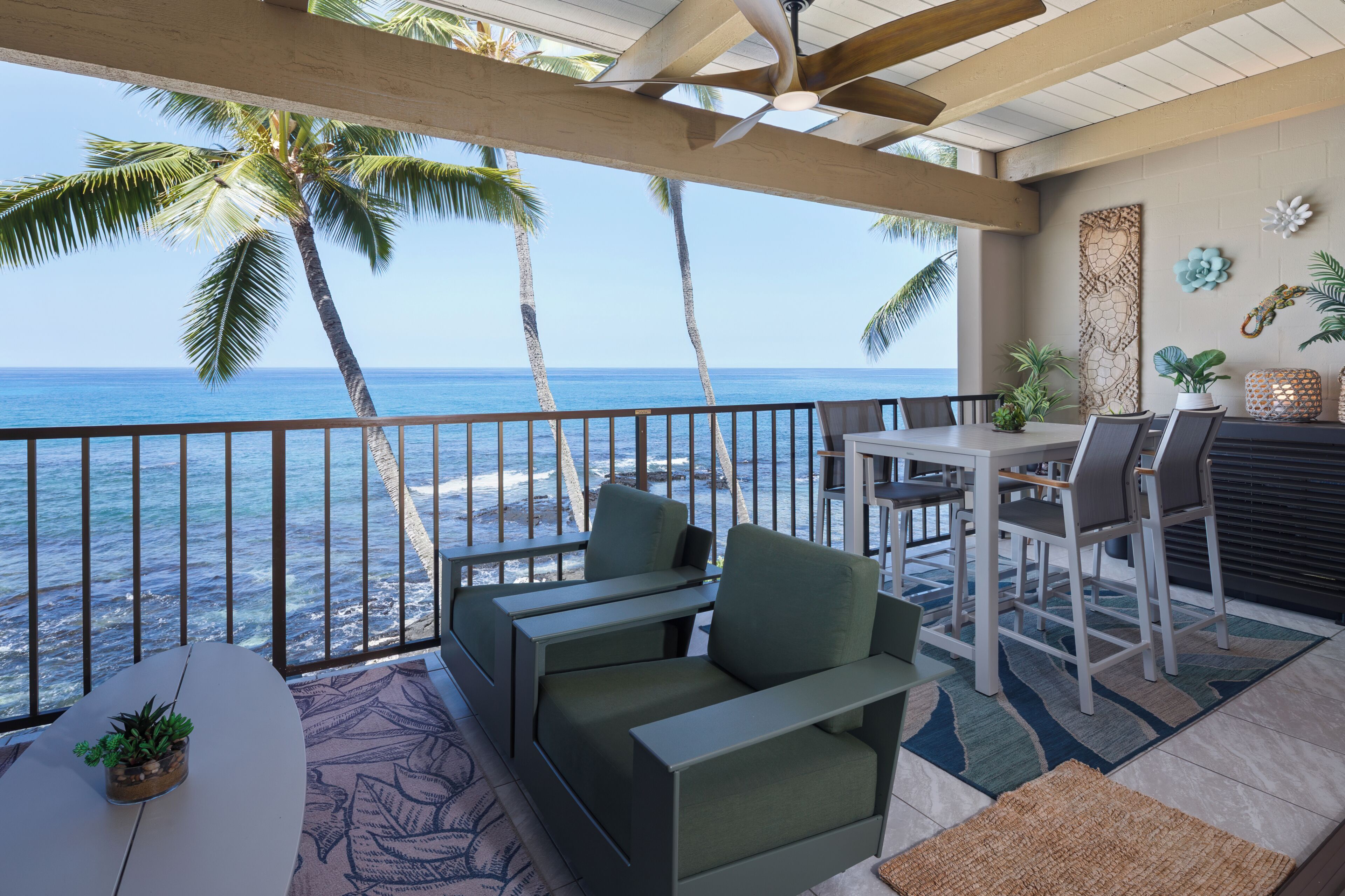 Un balcon avec vue sur l’océan, un coin repas avec des chaises et une table, et un espace détente avec des coussins.