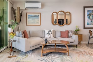 A modern living room with a sectional sofa, a coffee table, a large mirror, and a painting on the wall. - Beautiful Completely Renovated 2 Bed/2 Bath Oceanfront Gem - Kona Bali Kai #313 (Kailua-Kona)