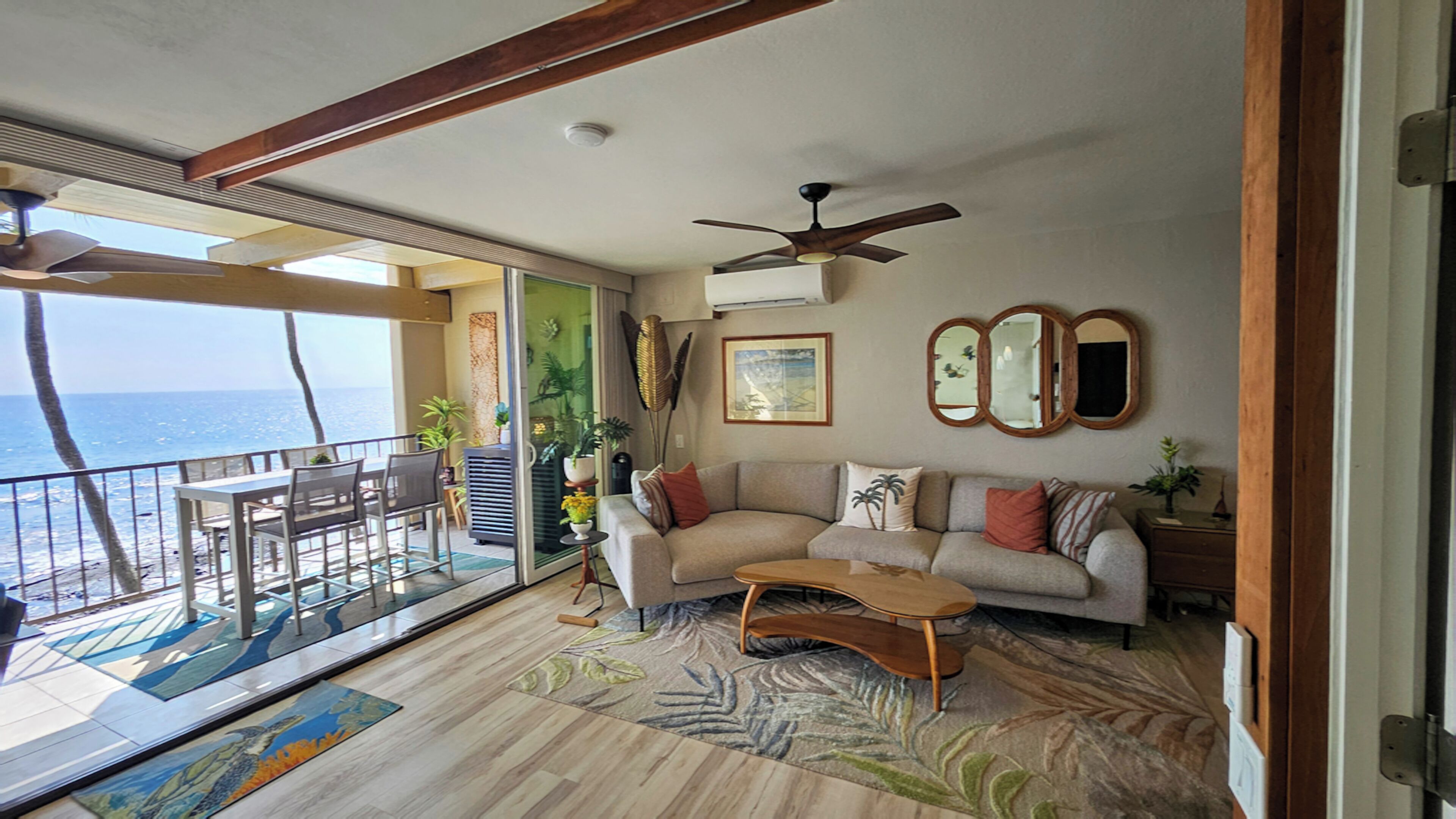 A living room with a sofa, coffee table, and a balcony with a view of the ocean.