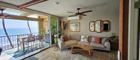 A living room with a sofa, coffee table, and a balcony with a view of the ocean.