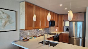 Une cuisine moderne avec des meubles en bois, des appareils électroménagers en acier inoxydable et des luminaires suspendus.