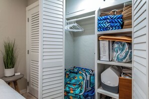 Un placard avec des portes coulissantes blanches, une tringle à vêtements, des serviettes pliées et une petite table sur laquelle est posée une plante en pot.