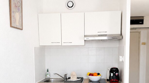 A compact kitchen with white cabinets, a stainless steel range hood, and a small countertop with a coffee maker and fruit bowl. - Le Thiers Azur AP4520 by Riviera Holiday Homes (Nice)