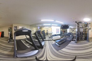 Een fitnessruimte met loopbanden, gewichten en een spiegelwand.