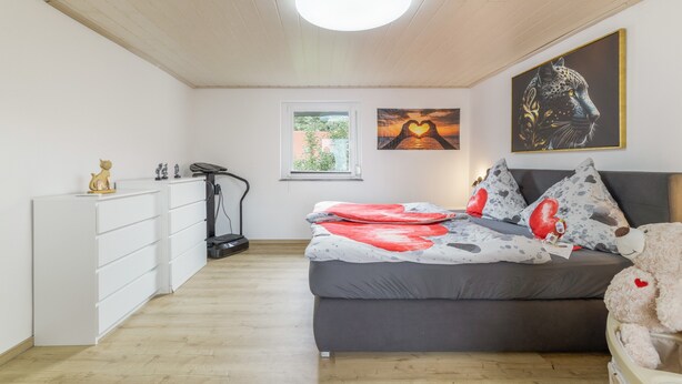 A bedroom with a bed, a treadmill, and artwork on the wall.