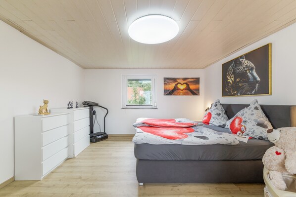 A bedroom with a bed, a treadmill, and artwork on the wall.