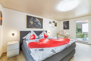 A bedroom with a bed, bedside tables, a nightstand, a window with a view, and wall art. - Apartment 'Am Fuße des Zoller' with Balcony and Wi-Fi (Bisingen)