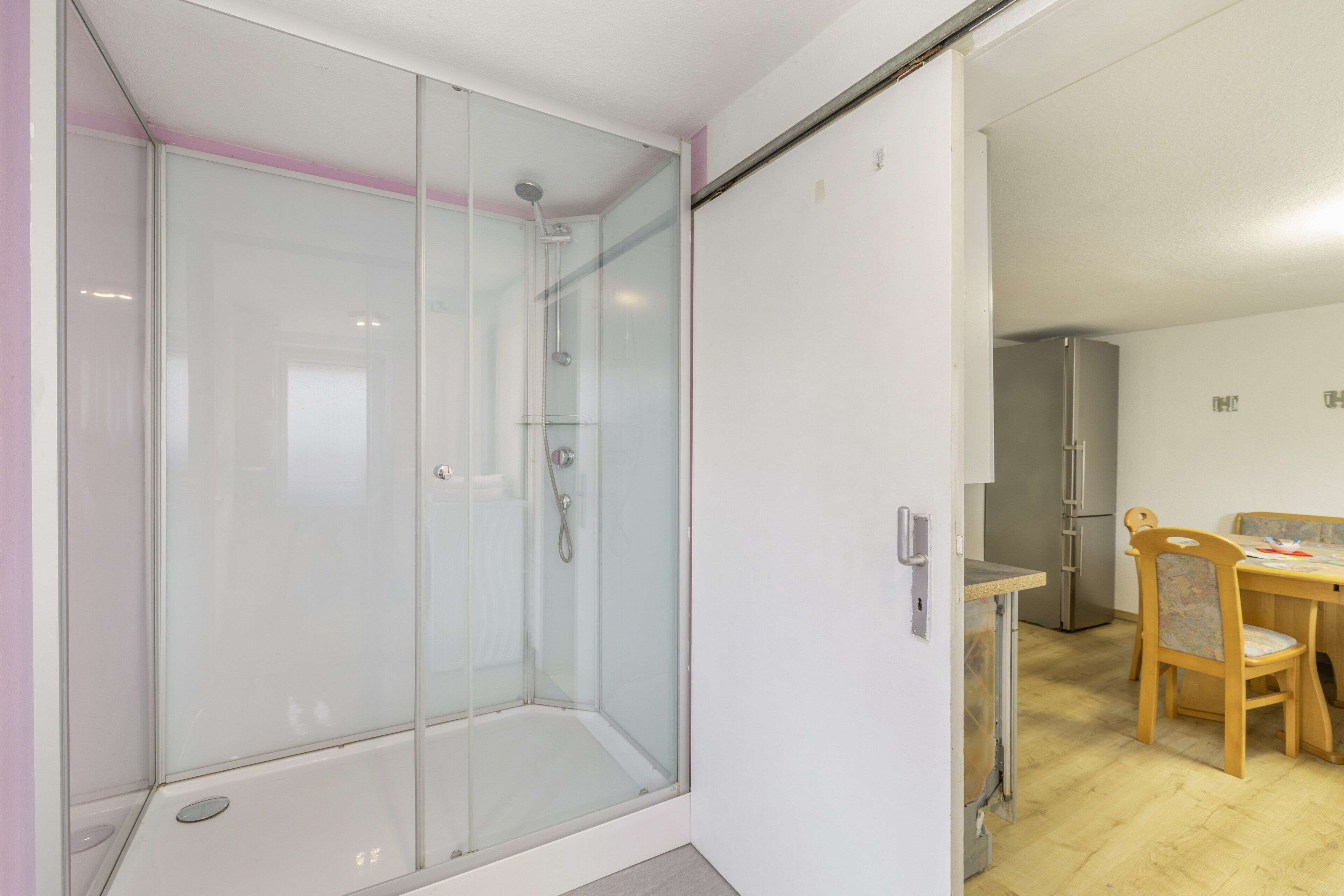 Ein modernes Badezimmer mit einer Duschkabine, ein Holztisch mit Stühlen und ein Kühlschrank.