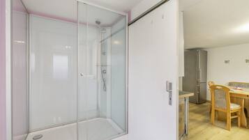 Ein modernes Badezimmer mit einer Duschkabine, ein Holztisch mit Stühlen und ein Kühlschrank.