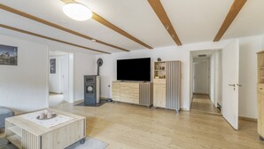 A modern living room with a flat-screen TV, wooden furniture, and a ceiling with exposed beams.