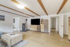 A modern living room with a flat-screen TV, wooden furniture, and a ceiling with exposed beams.