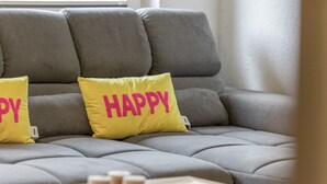 A grey sofa with two yellow pillows, one with 'HAPPY' and the other with 'DY'.
