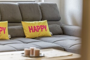 A grey sofa with two yellow pillows, one with 'HAPPY' and the other with 'DY'.