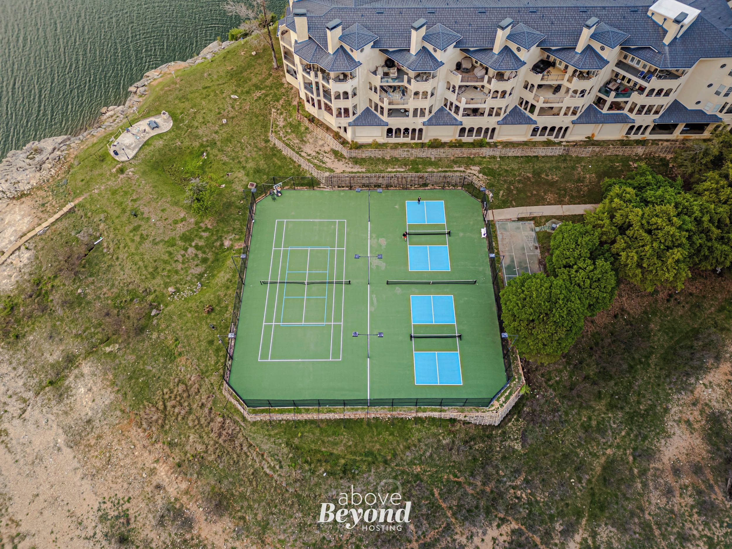 An aerial view of a tennis court surrounded by a large building with multiple balconies.