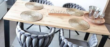 A dining table with four woven placemats, a wooden sign with text, and a set of glasses and a metal pitcher on a tray.