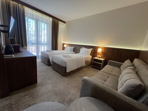A hotel room with two beds, a desk, a sofa, and a lamp.