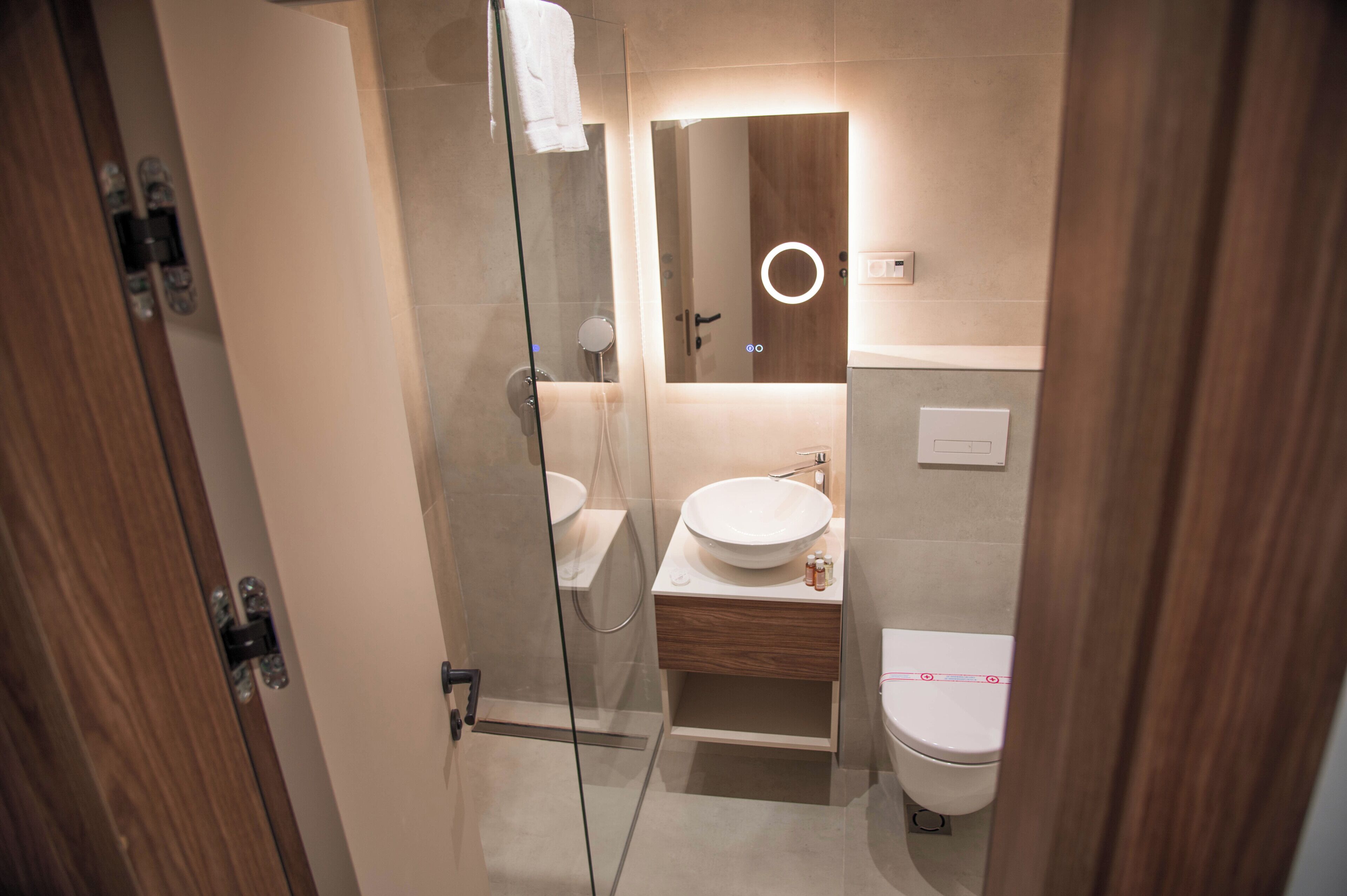 A modern bathroom with a glass shower enclosure, a wooden vanity, and a toilet.