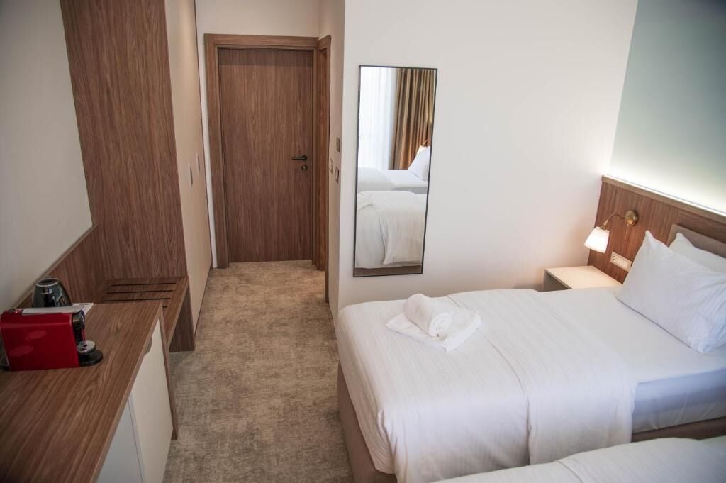 A hotel room with a bed, bedside table, a mirror, and a door leading to another room.