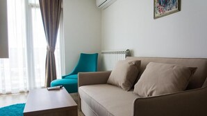 A living room with a beige sofa, a teal armchair, a wooden coffee table, and a radiator. - Hotel Onogošt (Nikšić)
