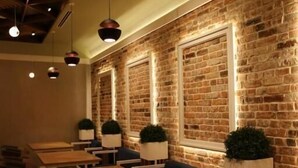 A restaurant with brick walls, hanging pendant lights, and wooden tables and chairs. - Hotel Onogošt (Nikšić)