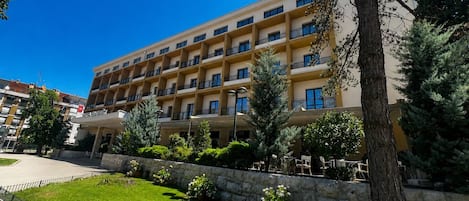 Un hotel de varios pisos con balcones, un patio empedrado y abundante vegetación circundante.