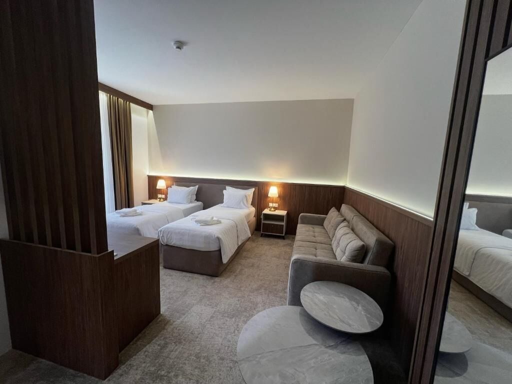 A hotel room with two beds, a sofa, a small table, and a mirror.