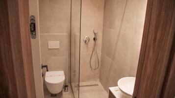 A modern bathroom with a glass-enclosed shower, a toilet, and a bidet.
