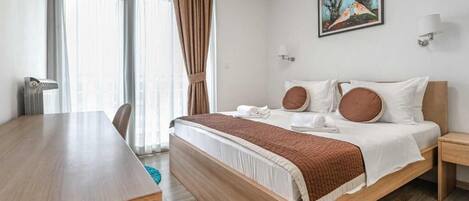Habitación de hotel con cama de madera, escritorio y ventana grande con cortinas.