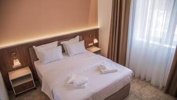 A hotel room with a bed, two bedside tables, a lamp, and a window with curtains.