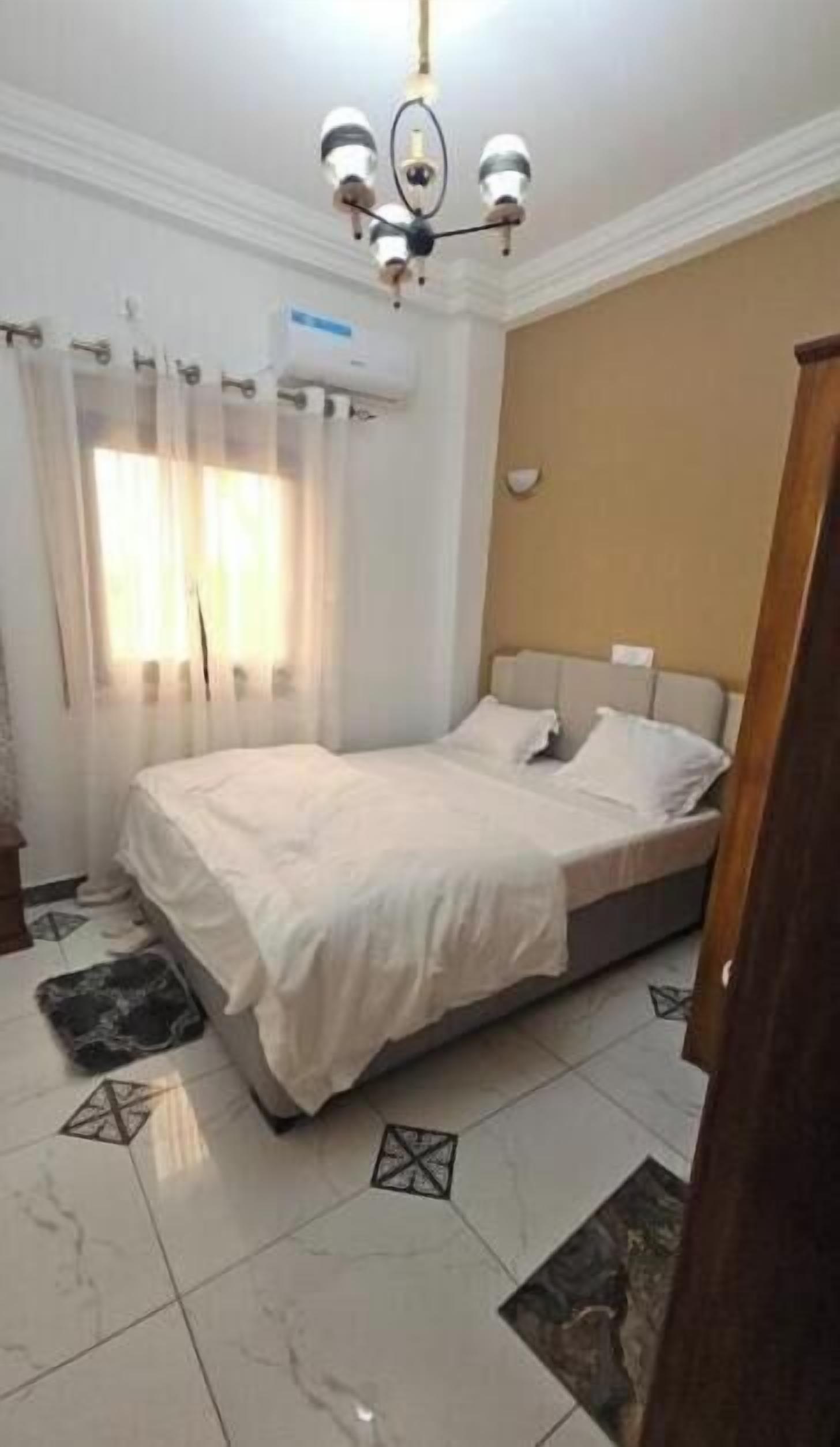 Un dormitorio con cama, lámpara de techo, ventana con cortinas y aire acondicionado de pared.