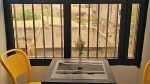 Ein Zimmer mit Tisch und zwei Stühlen, einem Fenster mit Gitter und Blick auf einen Außenbereich.