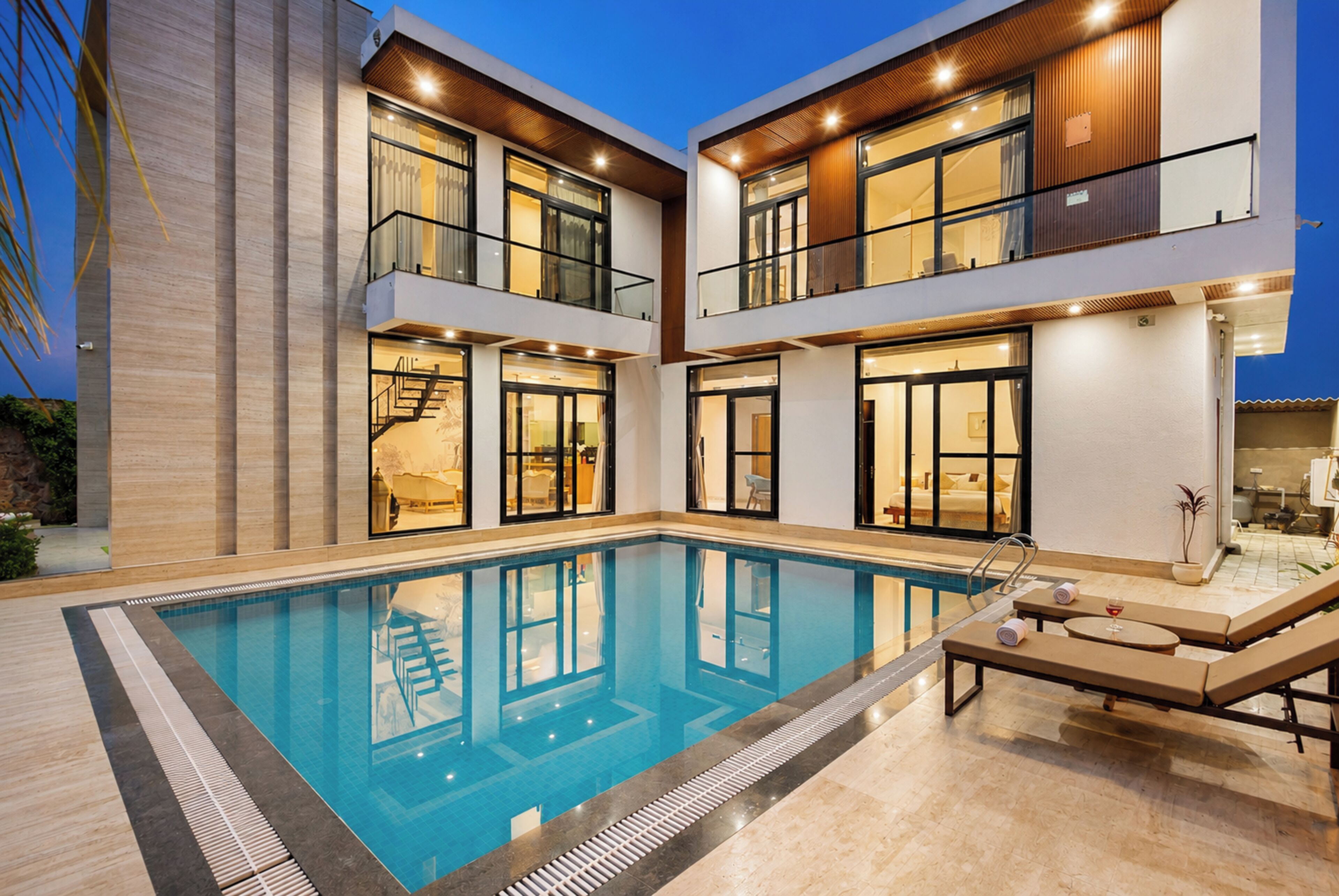 A modern two-story building with a swimming pool, outdoor seating, and a staircase leading to the upper floor.