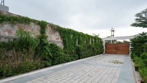 Een verhard pad dat leidt naar een toegangspoort met een bakstenen muur en beplanting aan de zijkant.
