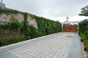 A paved pathway leading to a gated entrance with a brick wall and greenery on one side.