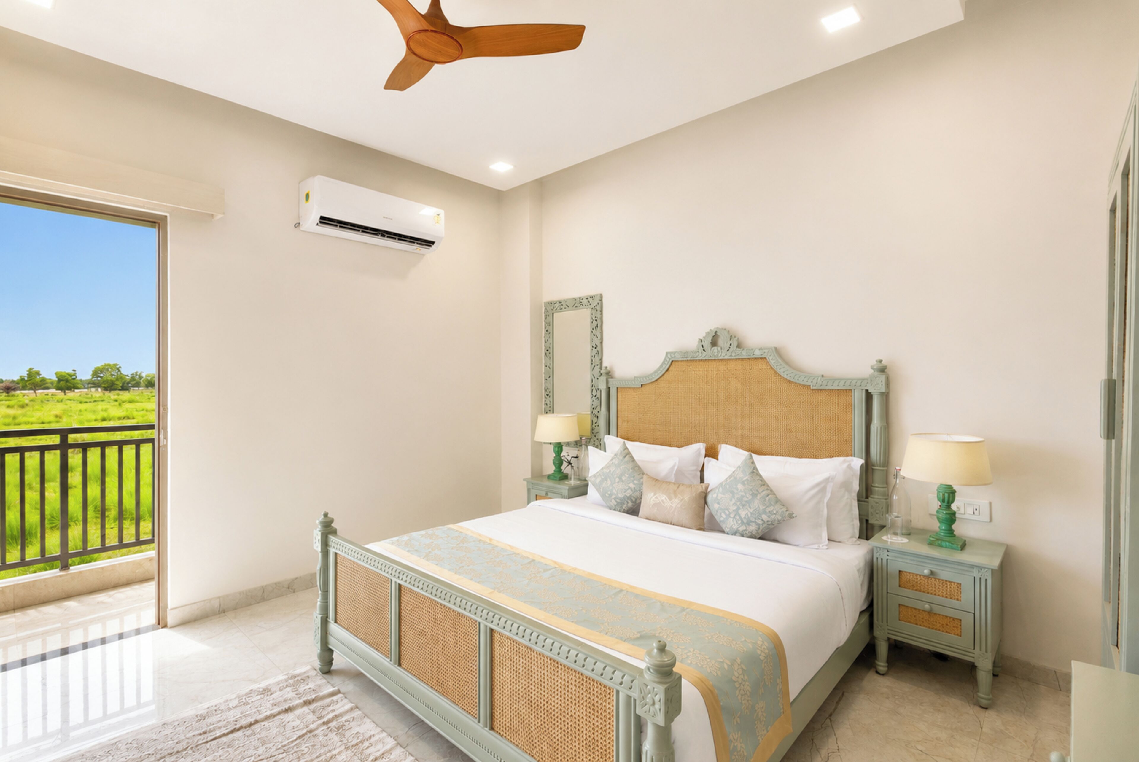 A bedroom with a large bed, two nightstands, a ceiling fan, an air conditioning unit, and a view of a green landscape.