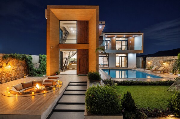 A modern two-story house with a swimming pool, outdoor seating, and a staircase leading to the upper floor.