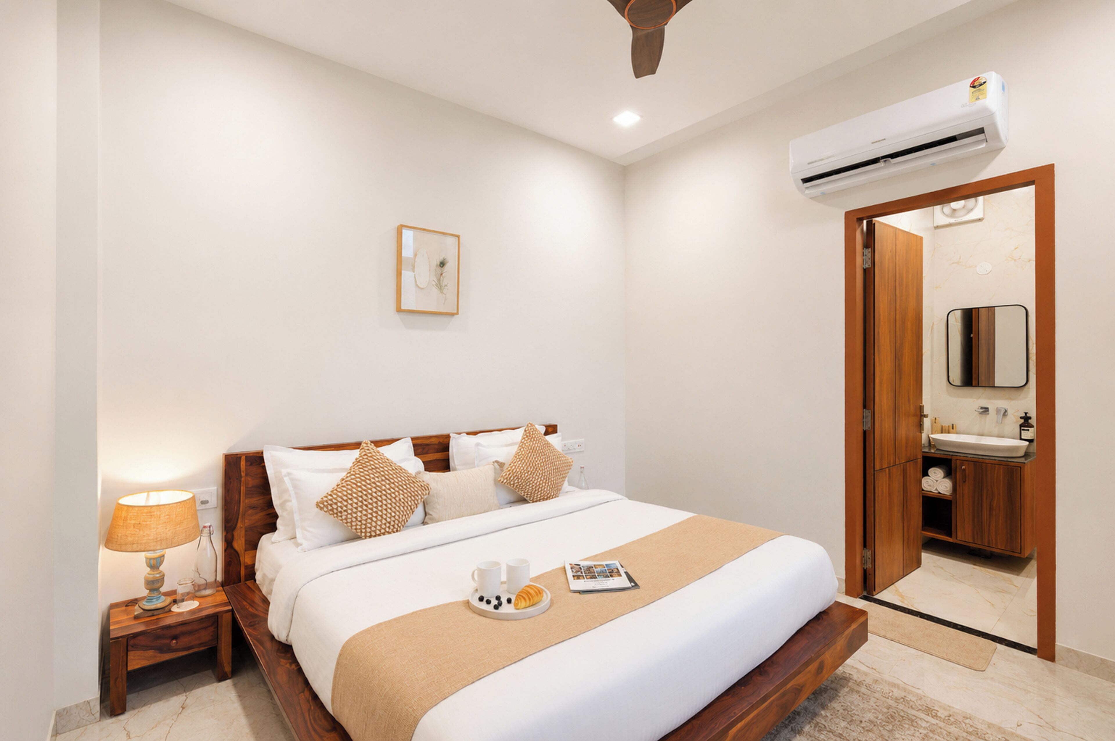 A hotel room with a bed, bedside table, lamp, and a bathroom with a mirror and sink.