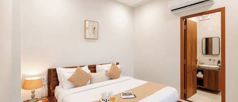 A hotel room with a bed, bedside table, lamp, and a bathroom with a mirror and sink.