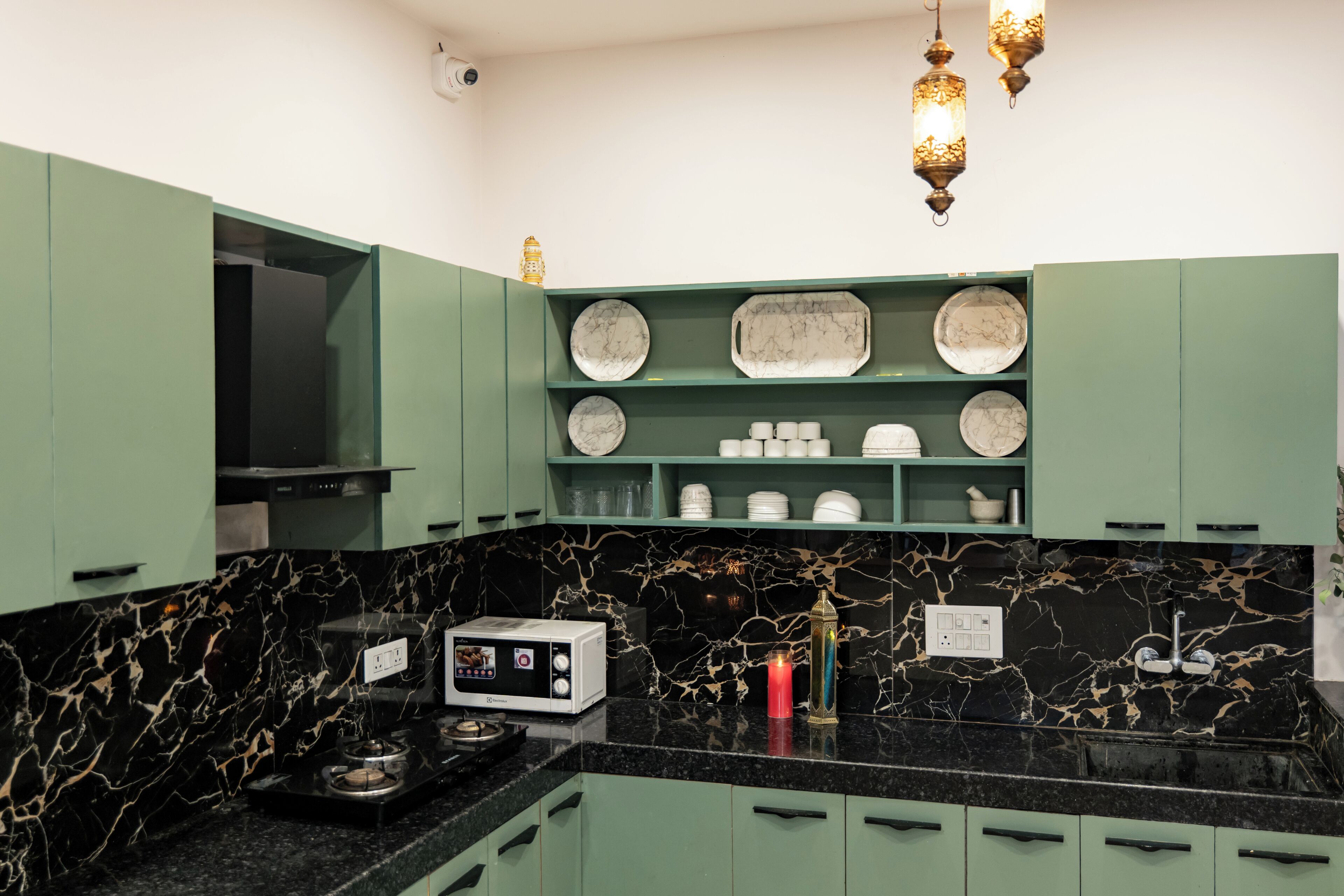 A kitchen with green cabinets, a black marble countertop, and a microwave.