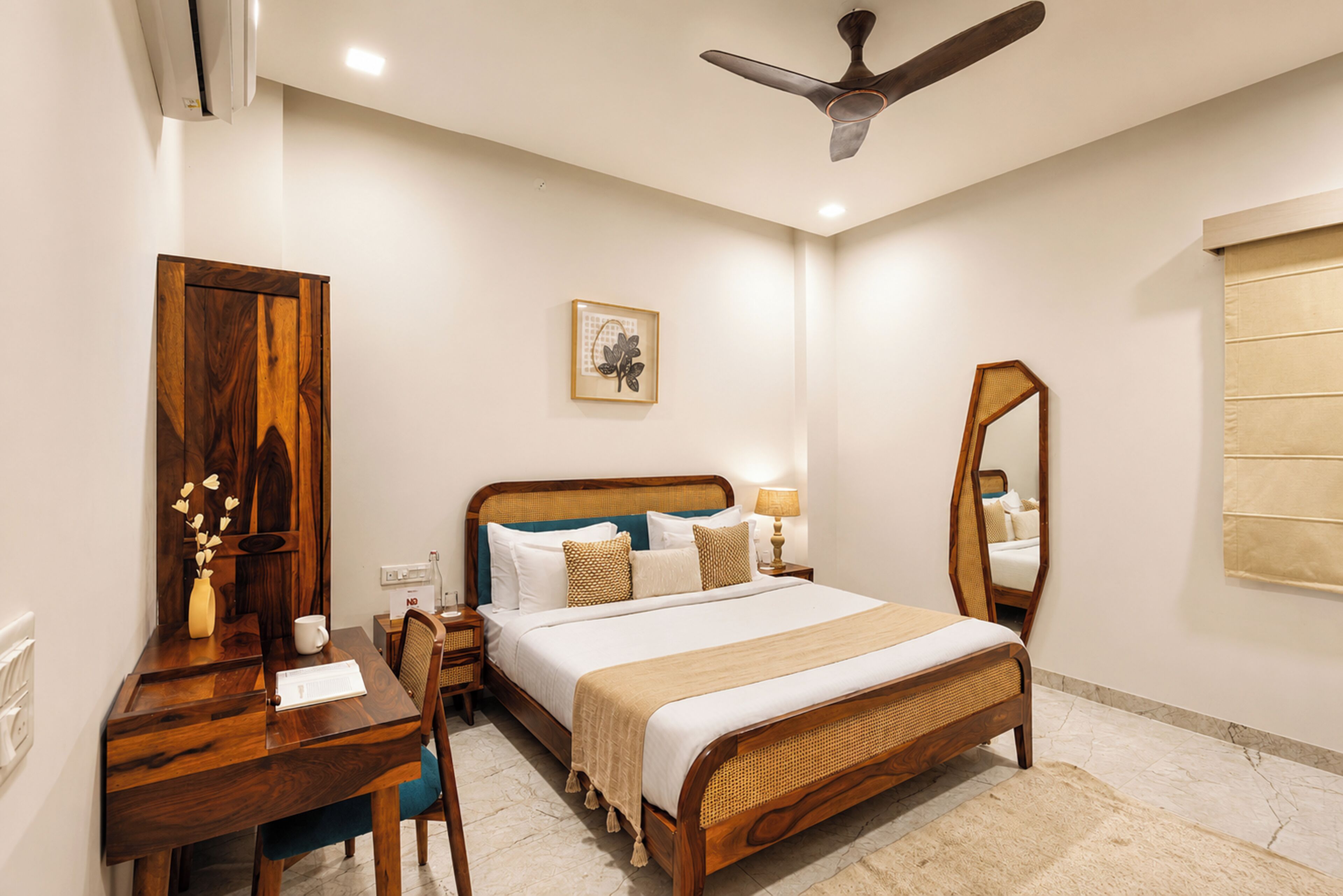 A bedroom with a bed, bedside table, lamp, mirror, and a ceiling fan.