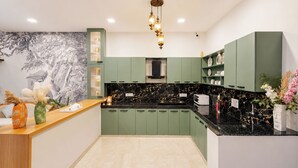 Een moderne keuken met groene kastjes, zwarte marmeren aanrechtbladen en een decoratieve lamp.