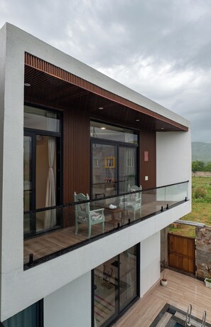 A modern two-story building with a balcony, large windows, and a view of the outdoors. - ELIVAAS Signature Angelos Farm 8BHK (Jaipur)