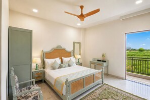 A bedroom with a bed, nightstands, a ceiling fan, a window with a view of greenery, and a door.