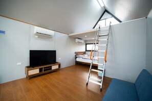 A compact room with a television, bunk bed, ladder, and built-in air conditioning unit.