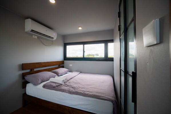 A bedroom with a bed, pillows, a window, and an air conditioning unit.